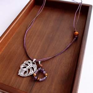 Macro view of hollow silver leaf pendant with purple bead and braided leather cord