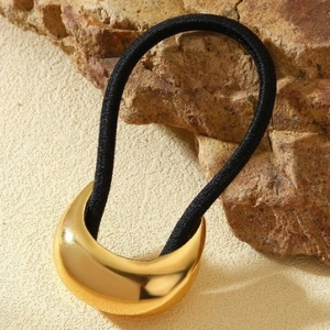 Black elastic hair tie with golden moon shaped metal charm on natural stone background