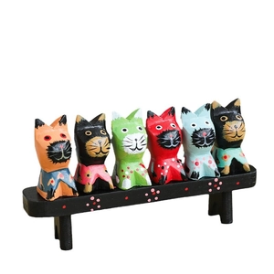 Set of six colorful hand-painted wooden cat figurines sitting on a black wooden bench stand