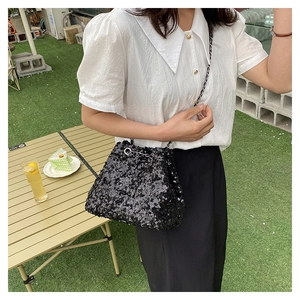 Detail of black sequin bucket bag featuring a woven chain strap and silver drawstring