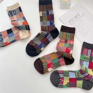 Close-up of four knitted crew socks with colorful patchwork plaid pattern and rich texture