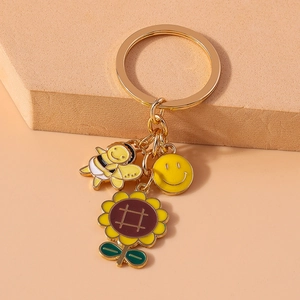 Detail of bee, sunflower, and smiley face charms on a golden enamel keychain