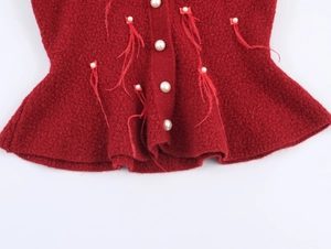 Dettaglio del cardigan in maglia rossa con bottoni di perle e frange piumate