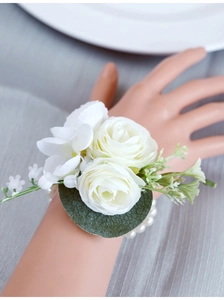 Close-up of white silk rose wrist corsage with green leaves and pearl bracelet