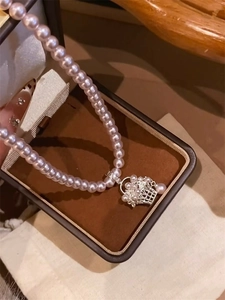 Close-up of pearl necklace featuring a detailed silver flower basket pendant over a jewelry box
