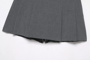 Close-up detail of dark grey pleated skirt fabric showing woven texture and sharp pleats