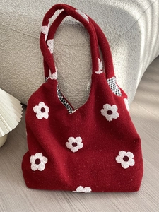Furry red tote bag with floral embroidery and checkered handle lining on a soft sofa