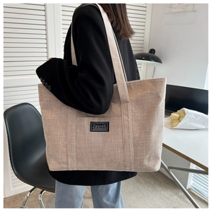Lifestyle view of large beige canvas tote bag with front pocket carried by a model