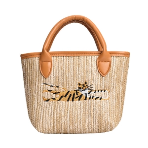 Straw woven bucket tote bag with brown leather handles and tiger embroidery on white background