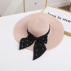 Detail of pink straw sun hat with a black ribbon bow and elegant pearl embellishments