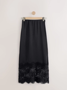 Detailed view of the black satin midi skirt featuring delicate lace patchwork on the hem