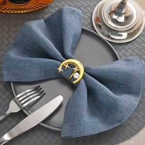 Detailed view of a gold moon and star napkin ring with pearl on a blue linen cloth