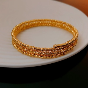 Detailed macro view of triple-layered gold bracelet with beaded texture and spherical ends