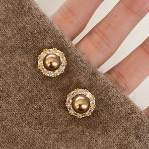 Close-up of champagne pearl stud earrings with zircon inlay on a cozy brown sweater