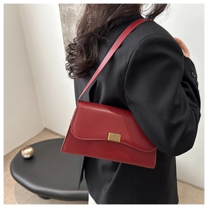Detail view of a vintage red leather underarm bag with a golden bar clasp on a black blazer