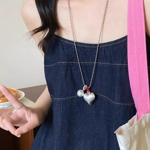 Long brushed silver heart pendant necklace with red bead and white bead on a model