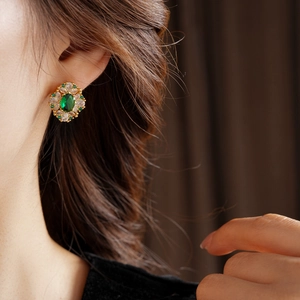 Gros plan sur une boucle d'oreille losange dorée avec pierre verte et détails en zircon