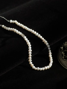 Macro detail of cream freshwater pearls on black velvet with silver chain necklace