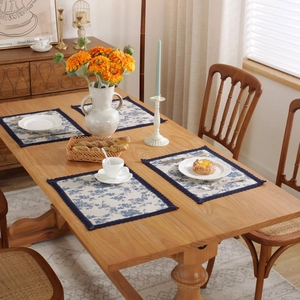 Detalle de mantel individual de lino azul floral con borde trenzado en mesa de madera