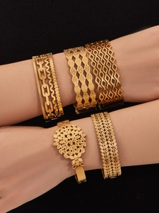 Detail view of five gold-plated hollow bangles with intricate vintage patterns on a model