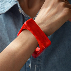 Detail of red marble pattern acrylic square bangle worn against a denim jacket