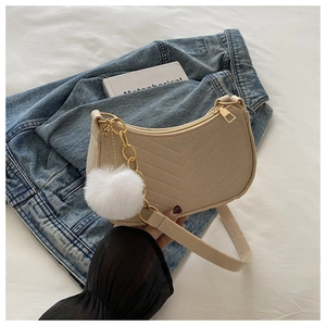Detalle de bolso media luna beige con acolchado en V y colgante de pompón blanco