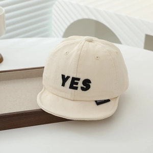 Close-up of a beige cotton baby baseball cap featuring black YES embroidery and short brim