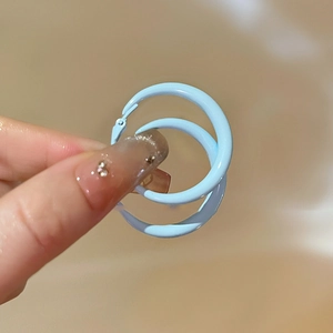 Close-up of a hand holding a light blue cream resin hoop earring for minimalist summer style