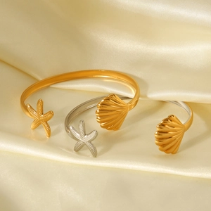 Detailed view of starfish and seashell charms on an adjustable gold stainless steel bangle