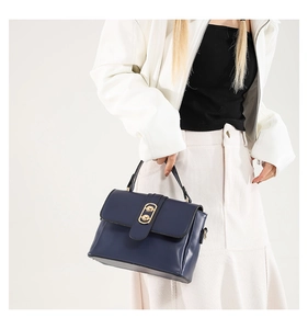 Detail of navy blue leather handbag featuring a polished gold oval metal clasp