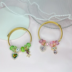Close-up of golden braided wire bracelets with green and pink crystal heart pendants