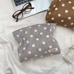Detailed texture of grey corduroy makeup bag with white polka dots on soft bedding