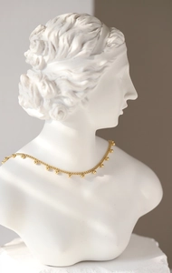 Close-up of golden beaded choker necklace on a plaster bust showing the elegant drape