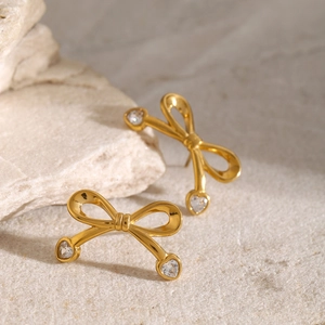 Macro detail of 18k gold plated bow earrings featuring heart-shaped zircon stones