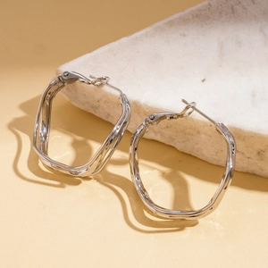 Close-up of silver irregular wavy geometric hoop earrings on white marble stone