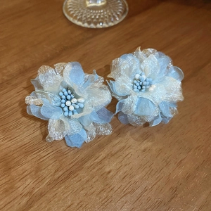 Detail shot of 3D mesh flower earrings with blue and silver petals on a wood surface