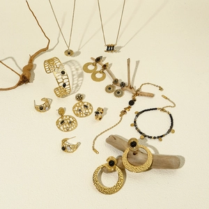 Flat lay of gold sunflower jewelry set with black stones on beige textured background