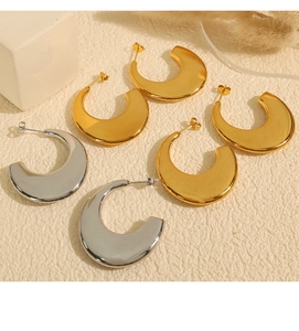 Close-up of broad C-shaped gold and silver earrings on textured background with decor