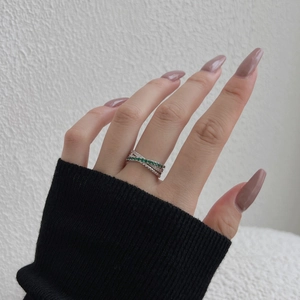 Detailed close-up of a silver crossover ring featuring small green zircon stones on a hand