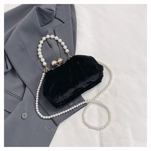 Detail of black plush handbag featuring a pearl handle and gold metal clasp on fabric