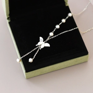 Macro shot of white butterfly pendant and freshwater pearl on a silver chain in box