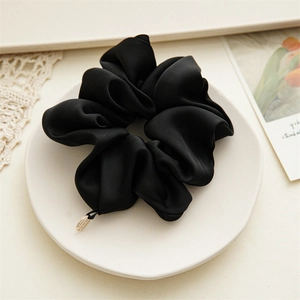 Detail of premium black satin scrunchie with soft silk texture and gold metal tag