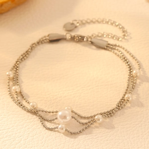 Detail of a triple-layer stainless steel bracelet featuring diverse white faux pearls