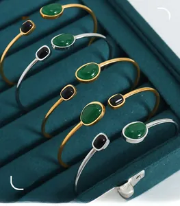 Detail view of five retro open bangles with green and black gemstones in a velvet box