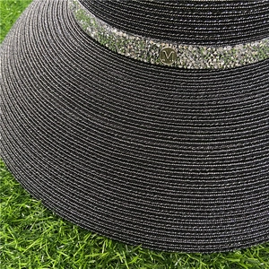 Detail of black woven sun hat with rhinestone band and gold M letter metal emblem