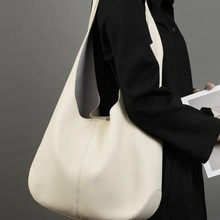Minimalistische cremeweiße Hobo-Tasche aus Leder mit Litschi-Textur an Model im schwarzen Mantel