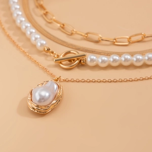 Macro detail of layered gold chain necklace featuring baroque pearl and T-bar toggle clasp