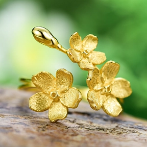Elegant gold flower ring with matte finish on rock base against a green background
