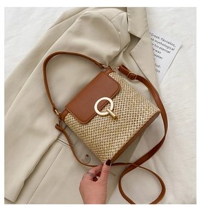 Detail of woven straw handbag with brown leather flap and gold ring lock on white blazer