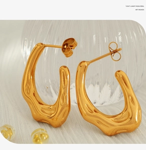 Close-up of golden irregular U-shaped earrings with lava hammer texture on white fabric